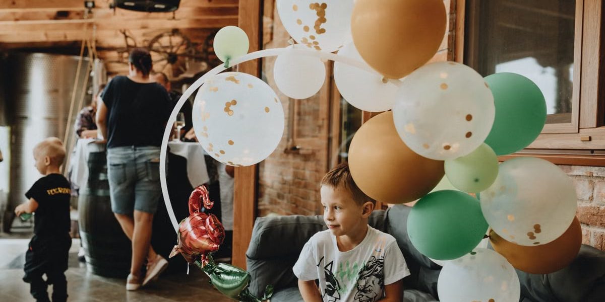 A young boy with balloons at an indoor birthday party gathering.