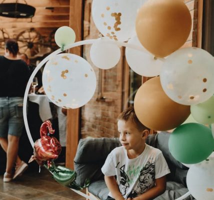 A young boy with balloons at an indoor birthday party gathering.